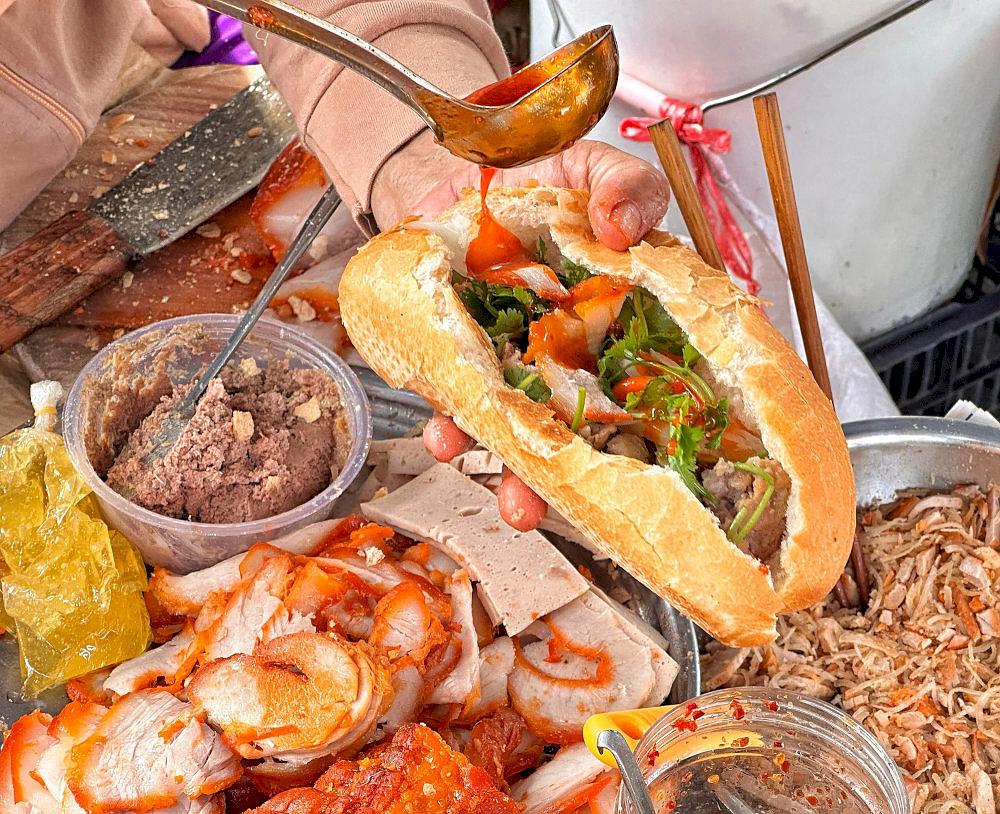 A crispy baguette (bạnh mi) filled with savory pork, pickled vegetables, and a rich sauce, perfect for a quick, flavorful meal